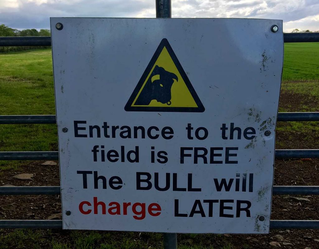 A sign warning people not to enter a field for fear of a bull charging.